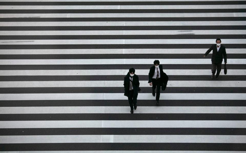 Commuters wearing masks walk across a pedestrian crosswalk Wednesday, Feb. 26, 2020, in Tokyo - Jae C. Hong / AP
