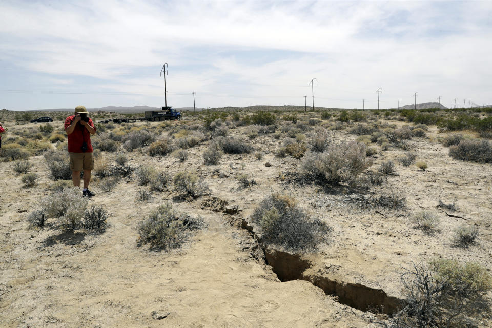 FILE - In this July 7, 2019 file photo, a visitor takes a photo of a crack in the ground following recent earthquakes in Ridgecrest, Calif., near the Naval Air Weapons Station China Lake military base. The base sustained heavy damage that experts estimate will cost nearly $5 billion to repair. (AP Photo/Marcio Jose Sanchez, File)