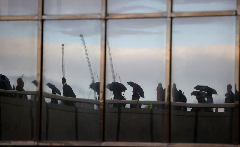 Commuters, reflected in windows of an office, walk across London Bridge toward the financial district, in London