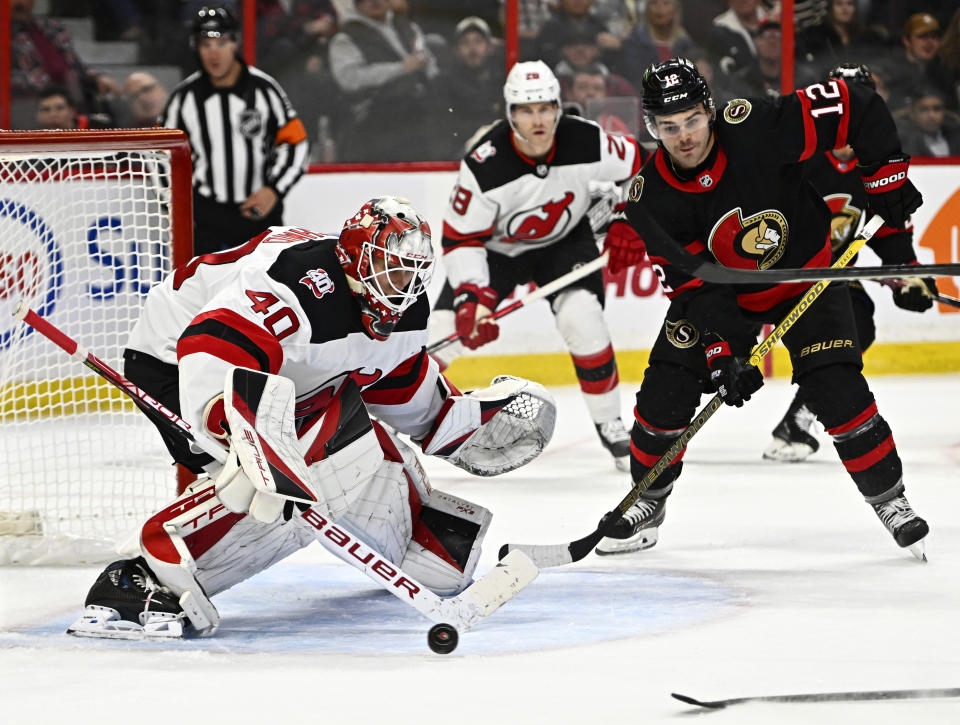 Ottawa Senators right wing Alex DeBrincat (12) watches the shot of centre Derick Brassard (61), not shown, in front of New Jersey Devils goaltender Akira Schmid (40) during the second period of an NHL hockey game in Ottawa, Ontario, on Saturday, Nov. 19, 2022. (Justin Tang/The Canadian Press via AP)