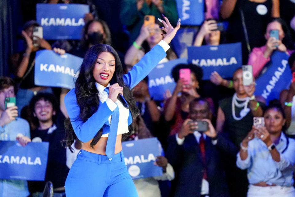 Megan Thee Stallion tritt in einem blauen Anzug vor einer Menschenmenge auf, die "Kamala" Zeichen