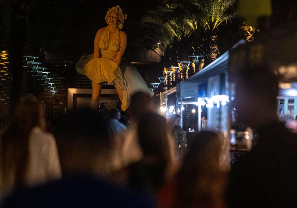 The Forever Marilyn statue watches from afar as VillageFest attendees explore various vendors in downtown Palm Springs, California, Thursday, May 9, 2024.