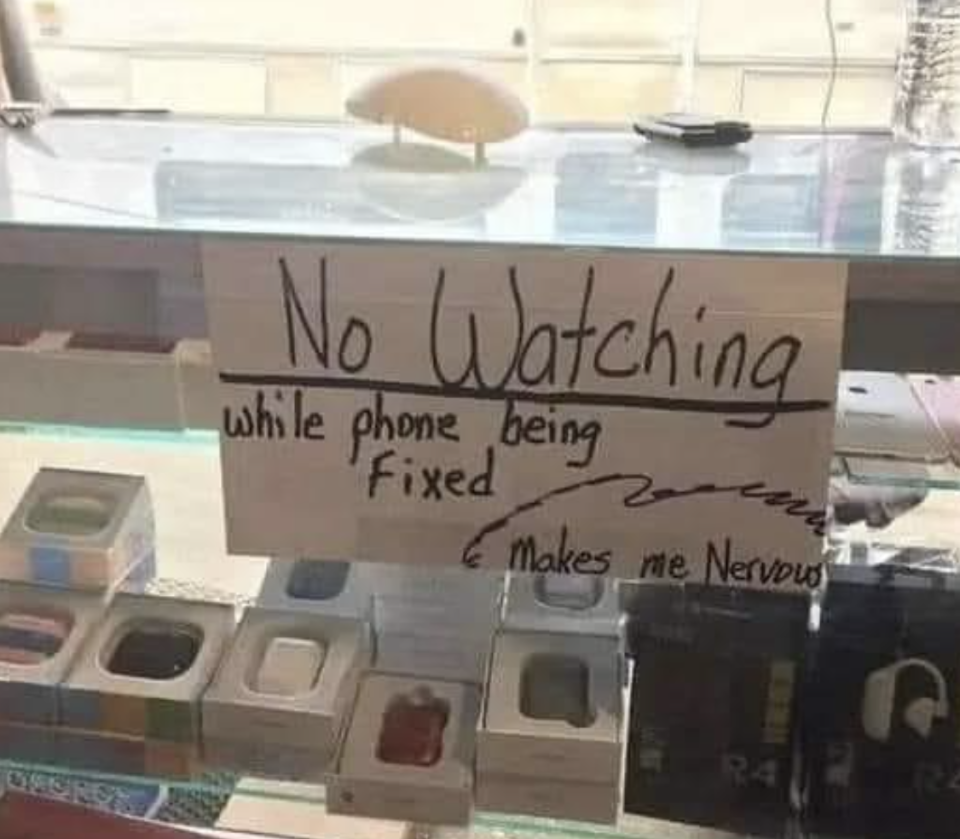 Sign on store counter reads "No Watching while phone being fixed, Makes me nervous," prohibiting observation of repairs