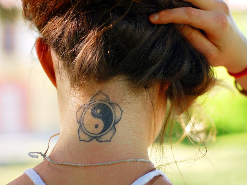 A woman lifts up her hair to show a flash tattoo of a ying and yang symbol