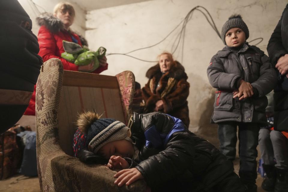 FILE - A child sleep in an armchair as other stand around in a shelter during Russian shelling, in Mariupol, Ukraine, Thursday, Feb. 24, 2022. As milestones go, the first anniversary of Russia's invasion of Ukraine is both grim and vexing. It marks a full year of killing, destruction, loss and pain felt even beyond the borders of Russia and Ukraine. (AP Photo/Evgeniy Maloletka, File)