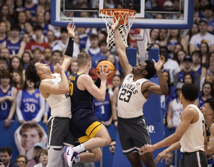 Kansas forward Jalen Wilson (10) and Kansas center Ernest Udeh Jr. (23) defend against a drive from West Virginia guard Erik Stevenson (10) during the first half of an NCAA college basketball game on Saturday, Feb. 25, 2023, at Allen Fieldhouse in Lawrence, Kan. (AP Photo/Nick Krug)