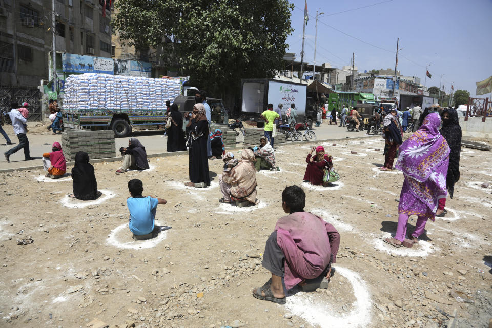 People sit at distance to receive relief goods during a nation-wide lockdown to contain outbreak of the coronavirus, in Karachi, Pakistan, Friday, March 27, 2020. The virus causes mild or moderate symptoms for most people, but for some, especially older adults and people with existing health problems, it can cause more severe illness or death. (AP Photo/Fareed Khan)