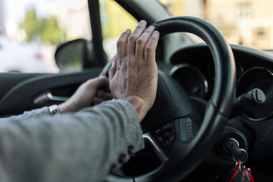 An image of a man's hand honking a horn on a car steering wheel