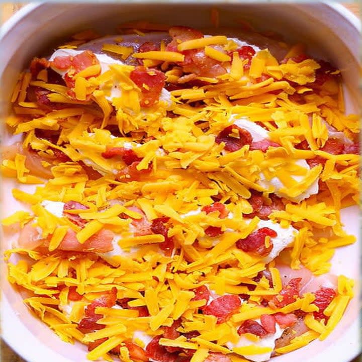 Chicken topped with shredded cheese and bacon in a baking dish.