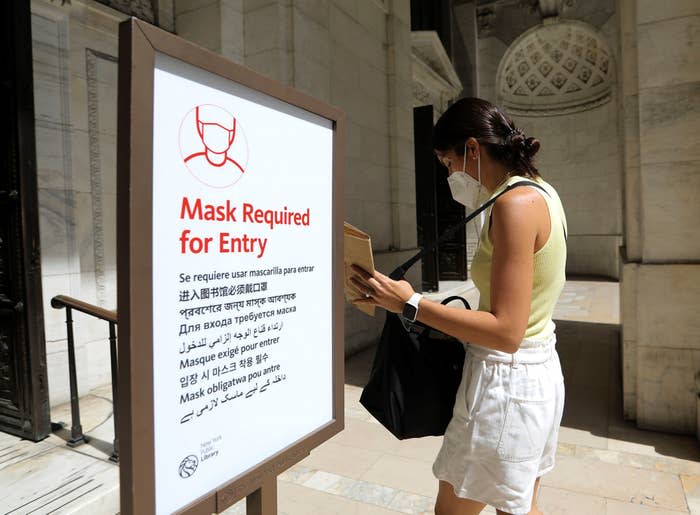 A woman in a face mask walks past a face mask requirement sign before entering the New York Public Library in New York City, on Aug. 2, 2021. 