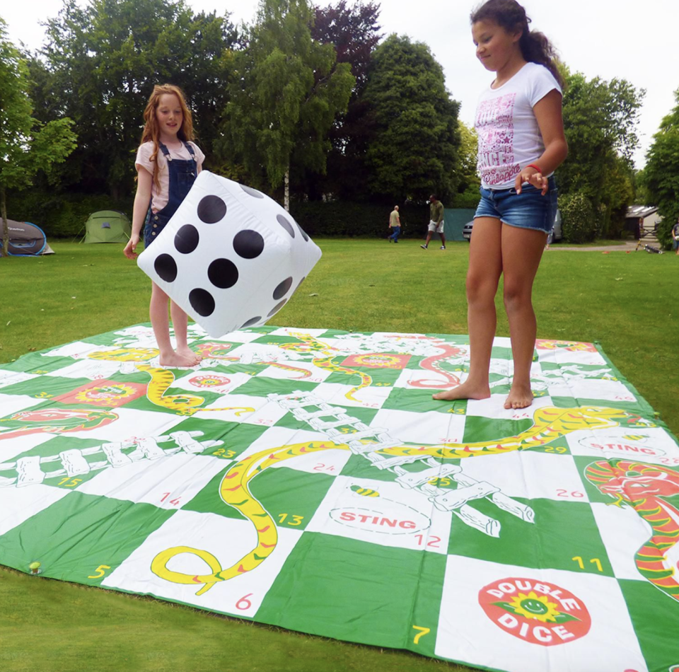 two girls playing on giant Big Game Hunters Snakes & Ladders Outdoor Board Game outside with giant dice (Photo via Walmart)