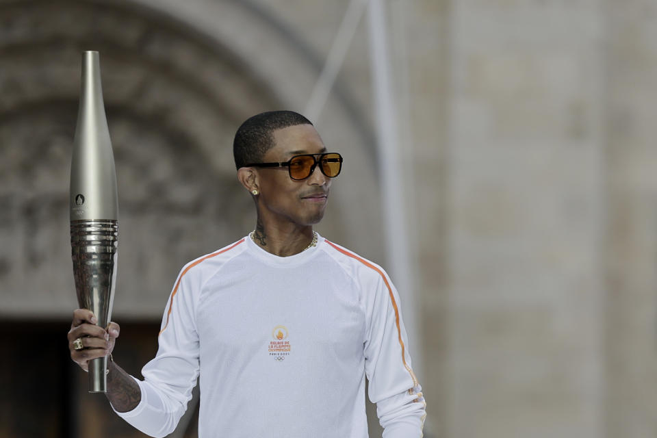 El rapero artista y diseñador Pharrell Williams sostiene la antorcha olímpica como parte del relevo de la antorcha de los Juegos Olímpicos de Verano de 2024 antes de la ceremonia de apertura en Saint-Denis, en las afueras de París, el viernes 26 de julio de 2024. (Stephane De Sakutin/Pool Photo via AP)