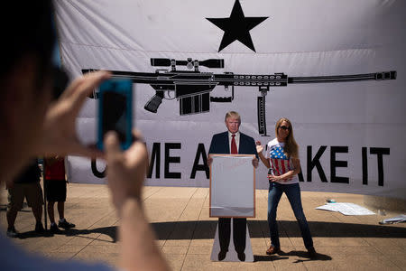 Bill Wang photographs his wife Brooke Wang as she sets a cardboard cutout of U.S. President Donald Trump in front of a banner during an open carry firearm rally on the sidelines of the annual National Rifle Association (NRA) meeting in Dallas, Texas, U.S., May 5, 2018. REUTERS/Adrees Latif