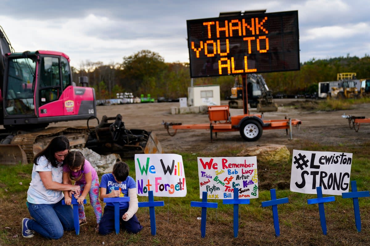 A family sit in front of signs honouring the lives lost in Lewiston’s mass shooting  (Copyright 2023 The Associated Press. All rights reserved.)