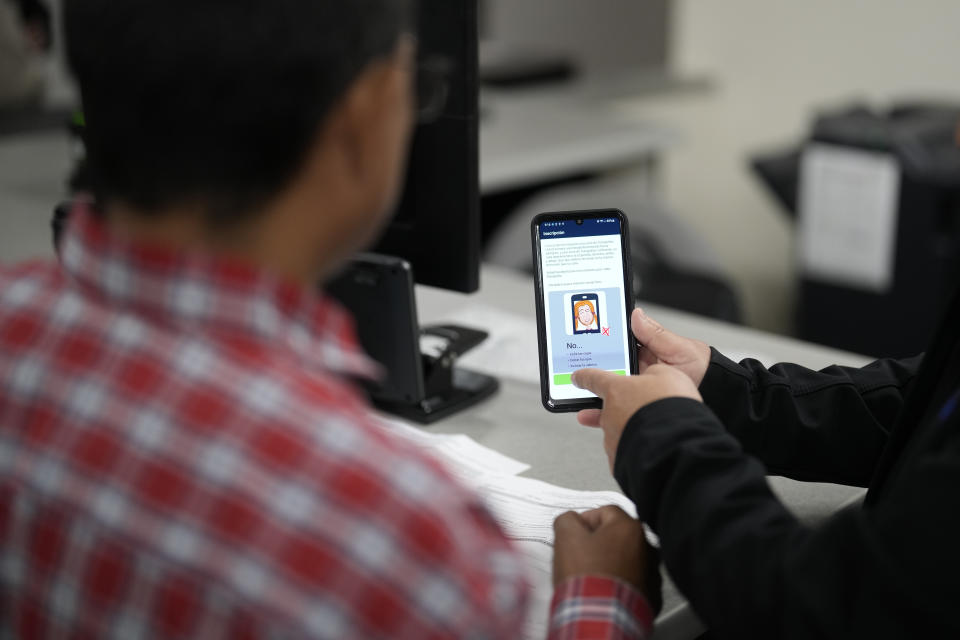 An officer helps set up a phone that will be used to track a man at an immigration and customs processing facility, Wednesday, March 15, 2023, in San Diego. Some asylum-seekers who crossed the border from Mexico are waiting 10 years just for a court date. The Border Patrol released people with notices to appear at a U.S. Immigration and Customs Enforcement office. The move saved the Border Patrol untold hours processing court papers, but it left the job to an agency that had no extra staff for the increased workload. (AP Photo/Gregory Bull)