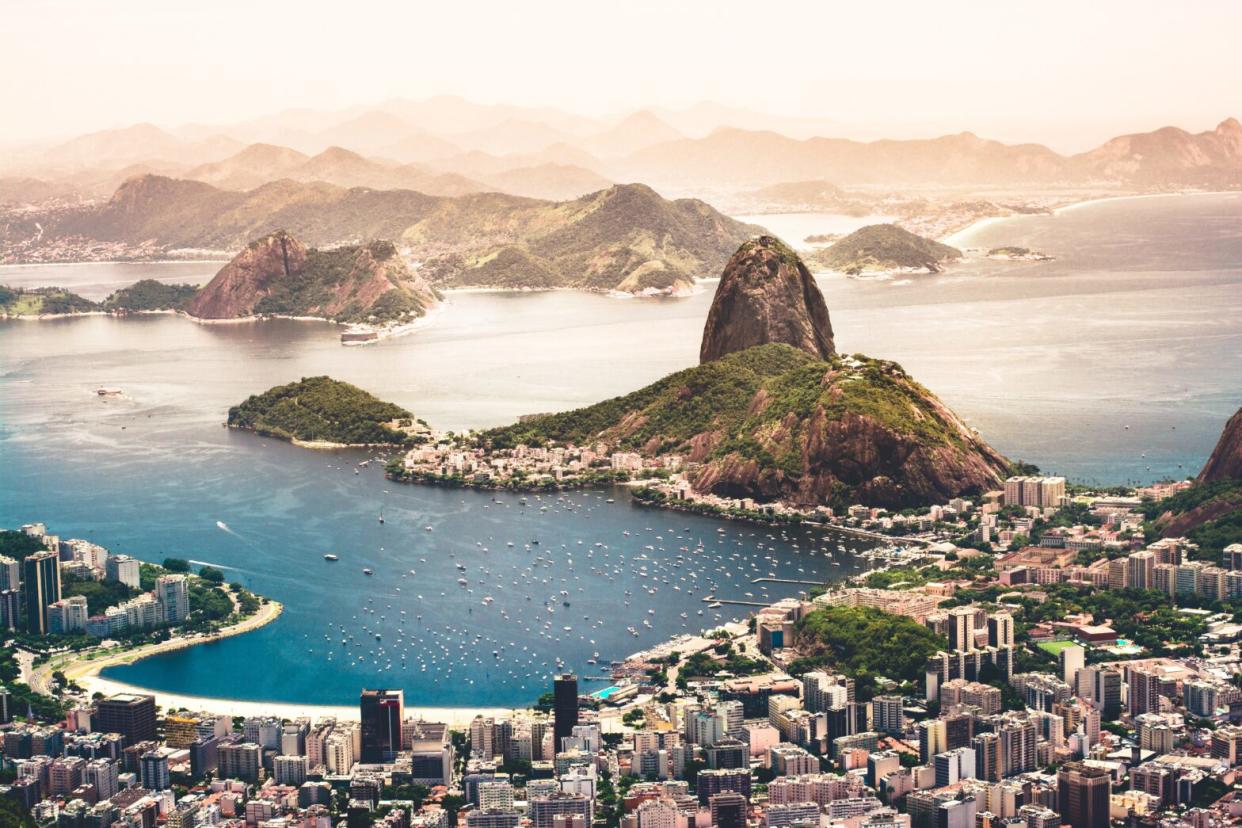 Rio de Janeiro is a city in Brazil that attracts millions of travelers each year. Check out how safe the destination is and what precautions travelers should take. pictured: A ocean view of Rio de Janeiro with bright blue waters and lush green lands