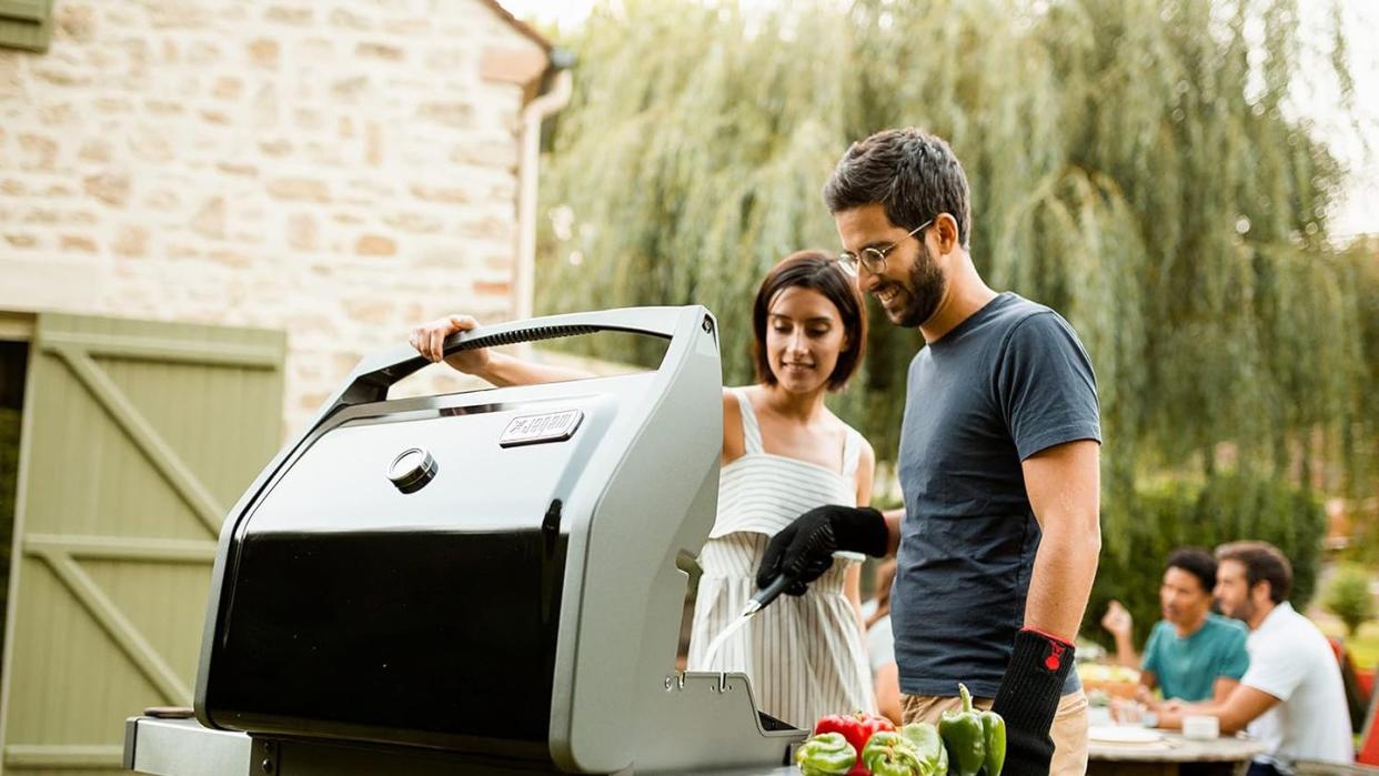 a man and woman standing next to a grill with food