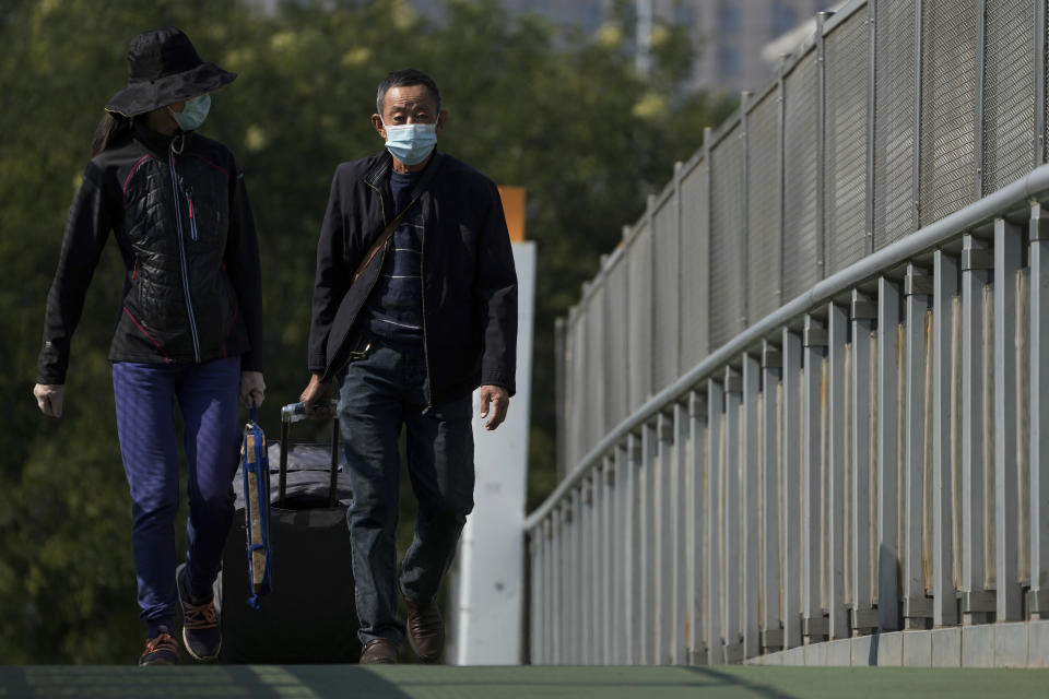 Traveller wearing face masks with their luggage walk on a pedestrian bridge near a train station in Beijing, Thursday, Oct. 6, 2022. Sprawling Xinjiang is the latest Chinese region to be hit with sweeping COVID-19 travel restrictions, as China further ratchets up control measures ahead of a key Communist Party congress later this month. (AP Photo/Andy Wong)