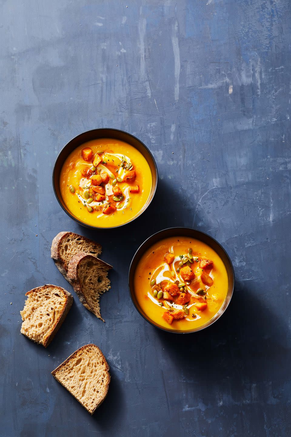 two bowls of butternut squash soup with slices of bread on the side