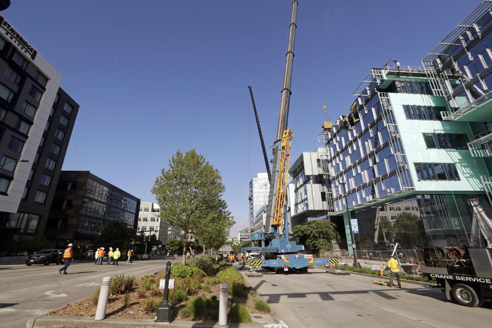 Workers, right, suspended in a basket survey the damage left on the building when the crane atop it collapsed a day earlier, striking both directions of Mercer Street below, Sunday, April 28, 2019, in Seattle. The construction crane fell from a building on Google's new campus during a storm that brought wind gusts, crashing down onto one of the city's busiest streets and killing multiple people. (AP Photo/Elaine Thompson)