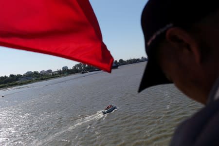 Man stands next to a Chinese flag fluttering on the Broken Bridge as a boat travels on the Yalu River separating North Korea and China, in Dandong