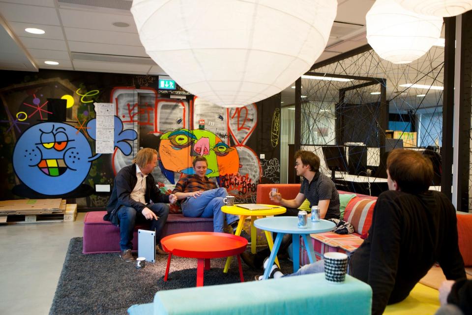 Employees sitting around tables in a colorful office space.