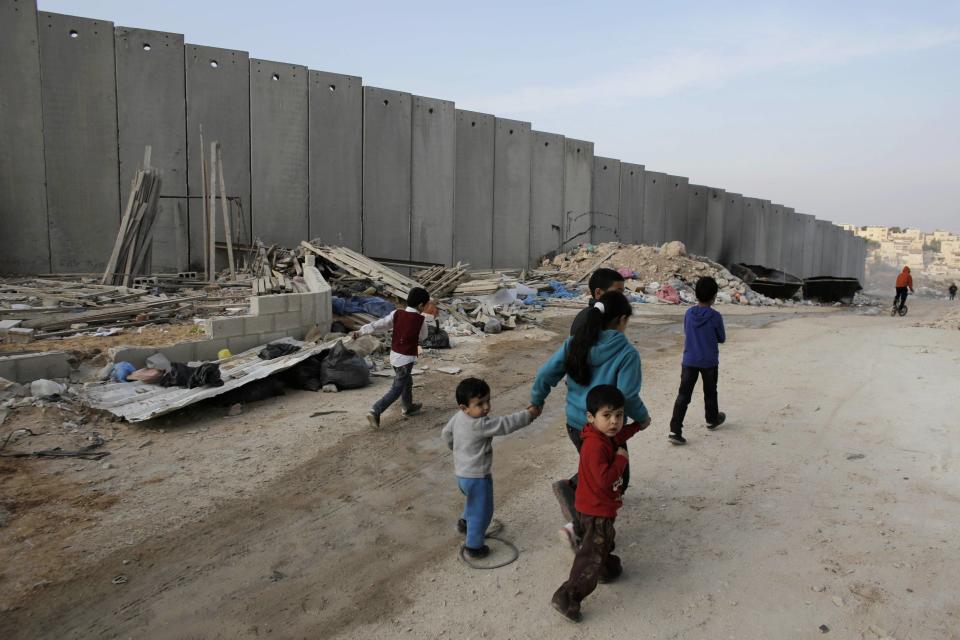 Palestinian children walk past garbage in Shuafat refugee camp in the West Bank near Jerusalem