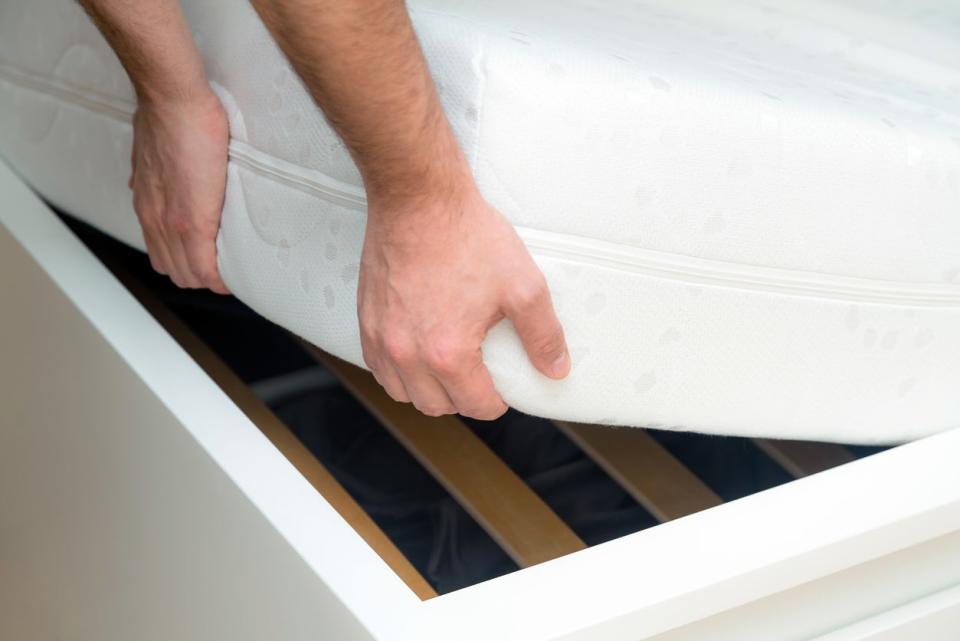 Man hands lifting the mattress at the bedroom. Looking at the bed frame, inspects the mattress