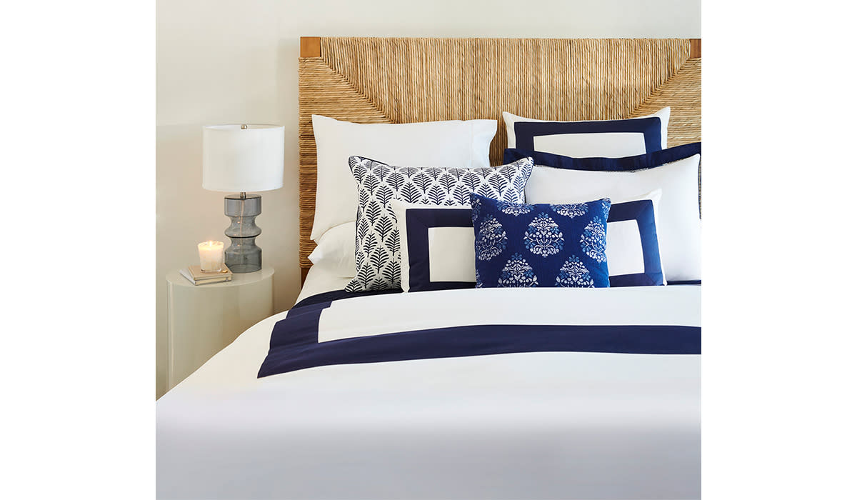 Blue and white bed with lots of patterned and solid pillows against a woven headboard