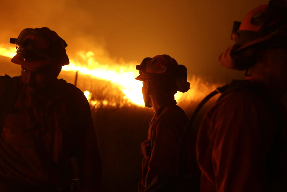 FILE - In this Sept. 12, 2015 file photo, California Department of Corrections and Rehabilitation inmates stand guard as flames from the Butte Fire approach a containment line near San Andreas, Calif. Attorneys representing 14 local governments said Tuesday, June 18, 2019 that they had reached a $1 billion settlement with California utility Pacific Gas & Electric for a series of fires dating to 2015. (AP Photo/Rich Pedroncelli, File)