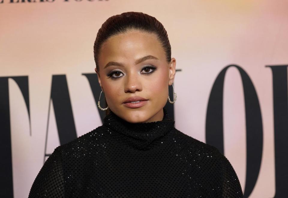 Sarah Jeffery poses in a sparkly black turtleneck against a pink backdrop.