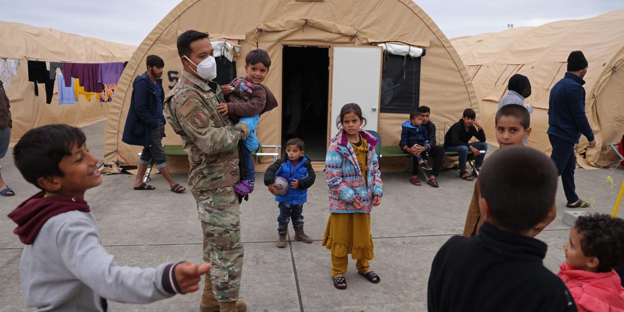 US soldier holds an Afghan child in front of refugee tents.