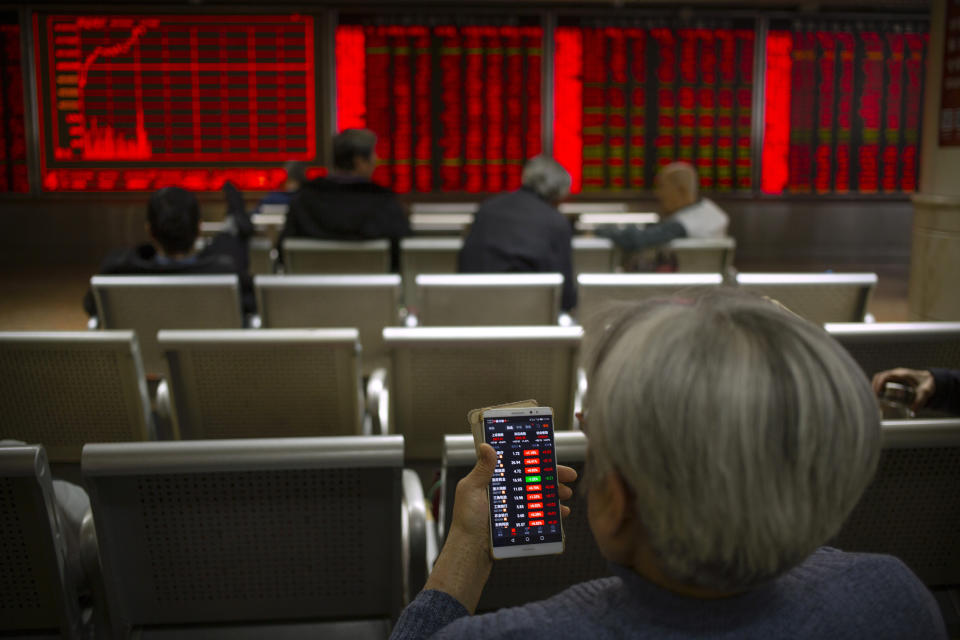 In this Tuesday, Nov. 19, 2019 photo, a Chinese investor uses a smartphone as she monitor stock prices at a brokerage house in Beijing. Shares retreated in Asia on Wednesday after Japan reported its worst monthly decline in exports in three years. (AP Photo/Mark Schiefelbein)