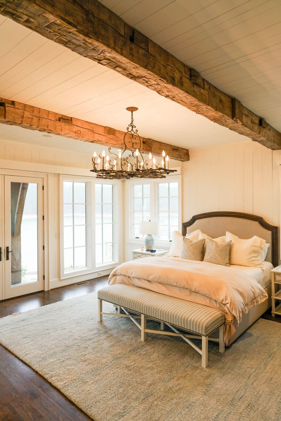 <p>Sophisticated neutrals are used throughout this charming bedroom, designed by <a href="https://deringhall.com/specialty-artisans/evolutia" rel="nofollow noopener" target="_blank" data-ylk="slk:Evolutia;elm:context_link;itc:0;sec:content-canvas" class="link ">Evolutia</a>. The traditional chandelier and hand-hewn beams give the space a country style.</p>