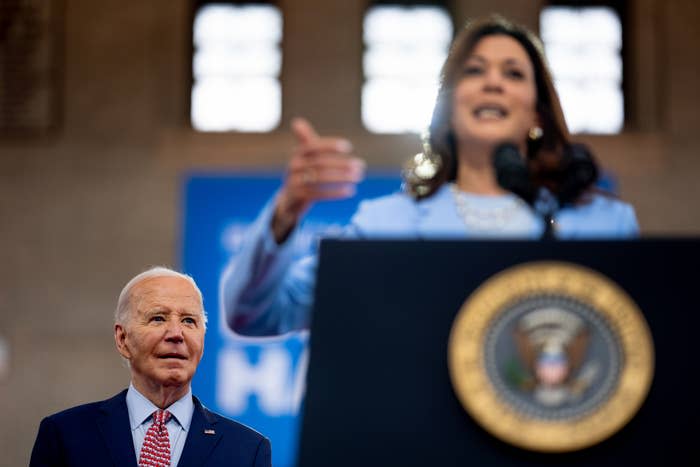 Joe Biden stands behind Kamala Harris who speaks at a podium with the presidential seal