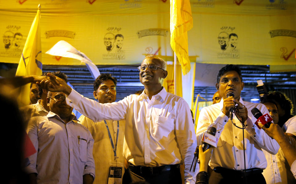 Maldives' opposition presidential candidate Ibrahim Mohamed Solih, center, shakes hands with a supporter as his running mate, Faisal Naseem, right, addresses the gathering in Male, Maldives, Monday, Sept. 24, 2018. A longtime but little-known lawmaker, Solih declared victory at his party's campaign headquarters in a contentious election widely seen as a referendum on the island nation's young democracy. (AP Photo/Eranga Jayawardena)