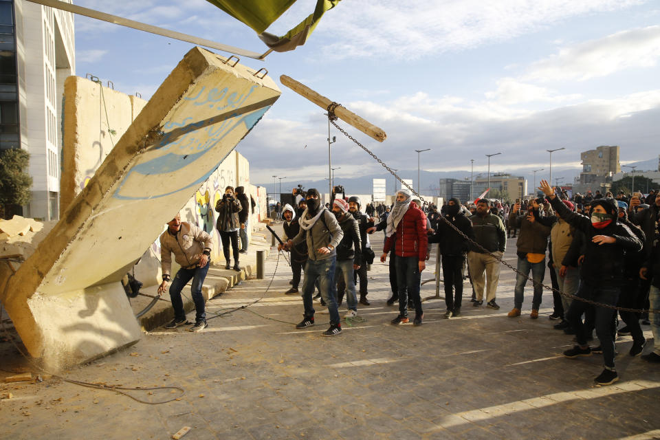 Protesters remove a concrete block from a wall that was installed by authorities to open a road that links to the parliament building during a protest against a parliamentary vote in downtown Beirut, Lebanon, Tuesday, Feb. 11, 2020. (AP Photo/Bilal Hussein)