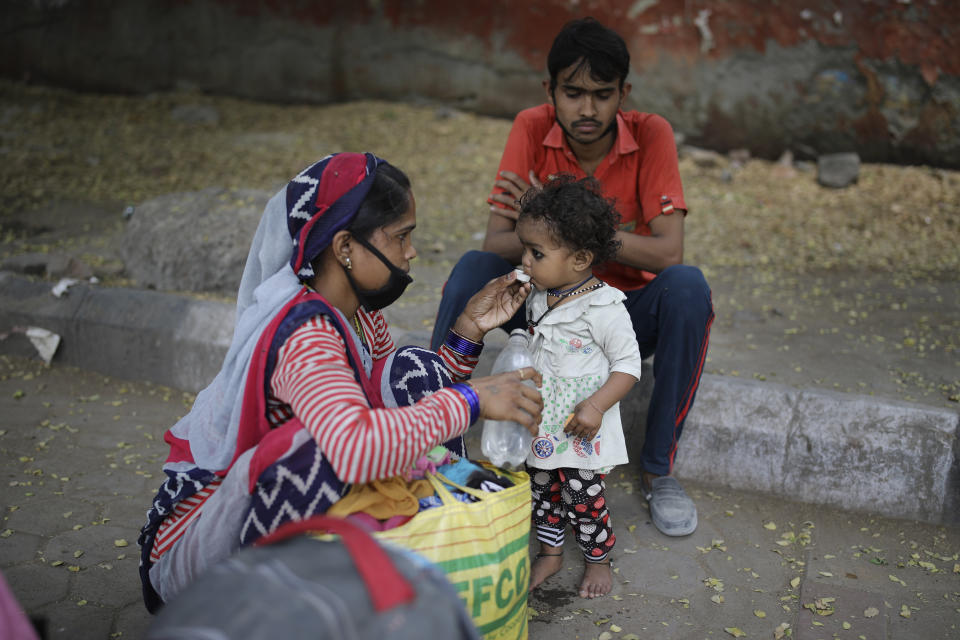 In this Wednesday, May 13, 2020, photo, the wife of a migrant worker gives water to her child as they rest briefly during their journey home, hundreds of miles away, on foot during a nationwide lockdown to curb the spread of new coronavirus in New Delhi, India. Tens of thousands of hungry and jobless migrants have been on the move across India , walking on railway tracks , riding in trucks and holding protests to demand food and transport to return home.(AP Photo/Altaf Qadri)