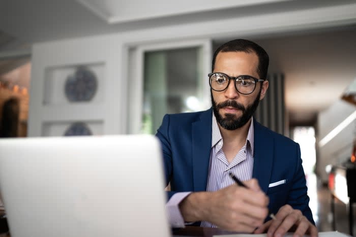 A person holding a pen while looking at a laptop computer. 