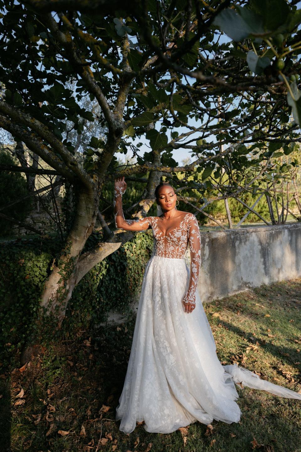 A bride closes her eyes and poses by a tree while wearing her wedding dress.