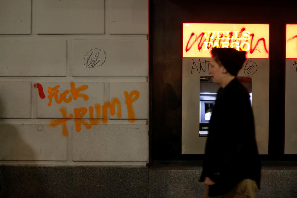 A pedestrian walks by a vandalized Wells Fargo bank office.