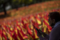 A woman sits near to the Spanish flags placed in memory of coronavirus (COVID-19) victims, in Madrid, Spain, Sunday, Sept. 27, 2020. An association of families of coronavirus victims has planted what it says are 53,000 small Spanish flags in a Madrid park to honor the dead of the pandemic. (AP Photo/Manu Fernandez)