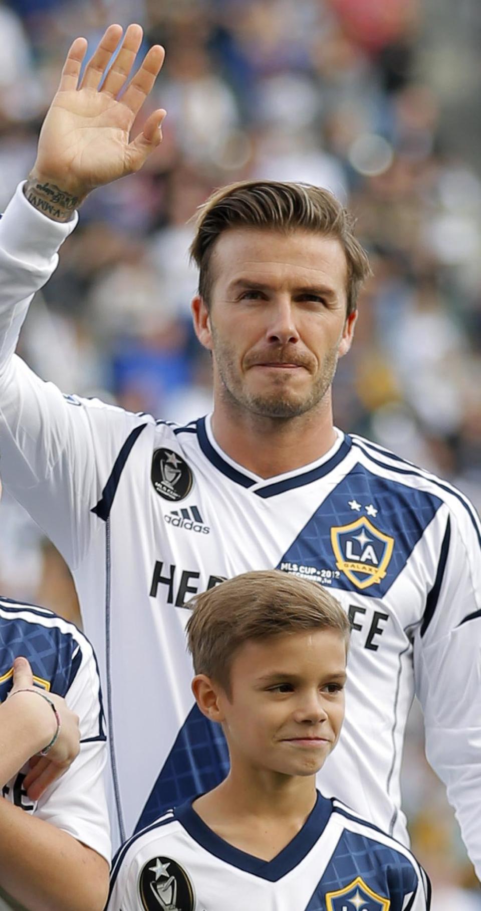 FILE- Los Angeles Galaxy's David Beckham, of England, waves as he stands with his son Romeo, in Carson, Calif., USA, in this file photo dated Saturday, Dec. 1, 2012. It is announced Tuesday Dec. 18, 2012 that the son of soccer star David Beckham and former Spice Girl singer Victoria Beckham, ten-year old Romeo Beckham, is the new face of the London based clothing brand Burberry and will feature in upcoming ads for Burberry’s spring/summer 2013 collection. (AP Photo/Jae C. Hong, FILE)