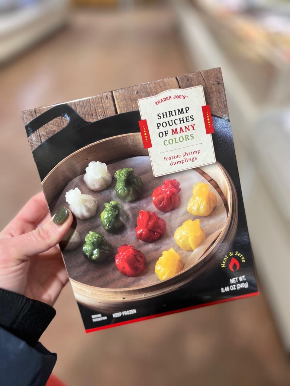 Hand holding a Trader Joe's Shrimp Dumplings package with colorful dumplings displayed on a plate