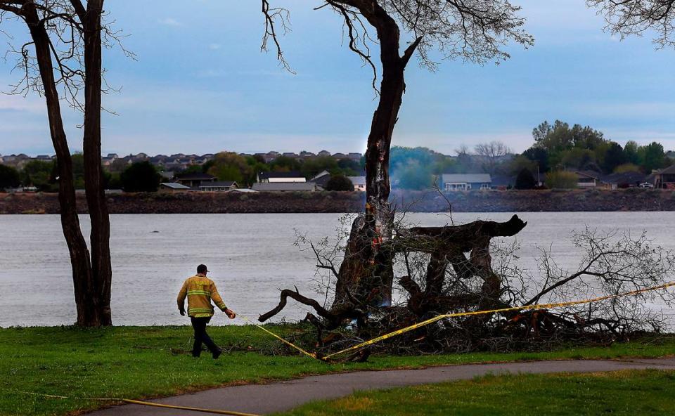 Capt. Tony Jorgensen of the Kennewick Fire Department strings caution tape around a burning tree the morning after a natural cover fire scorched a section of land between the roadway and river in Kennewick’s Columbia Park. The has partially collapsed and is in danger of crashing down completely.