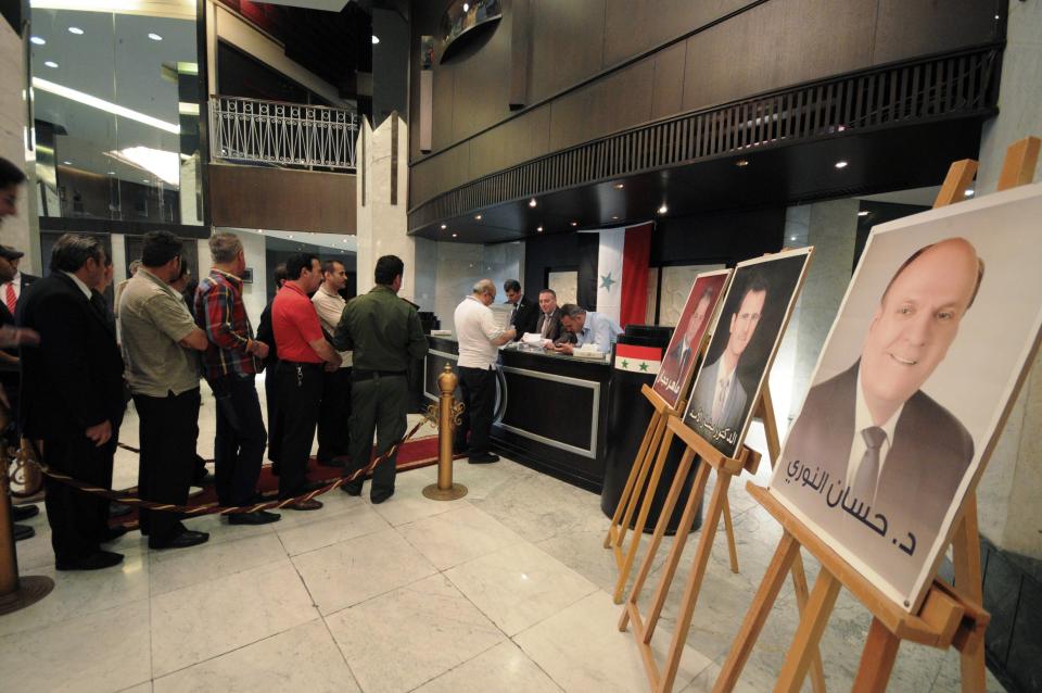 People queue to cast their votes in the presidential election near portraits of the candidates, including Syria's President Bashar al-Assad (C), at Dama Rose hotel in Damascus, June 3, 2014. (REUTERS/Omar Sanadiki)