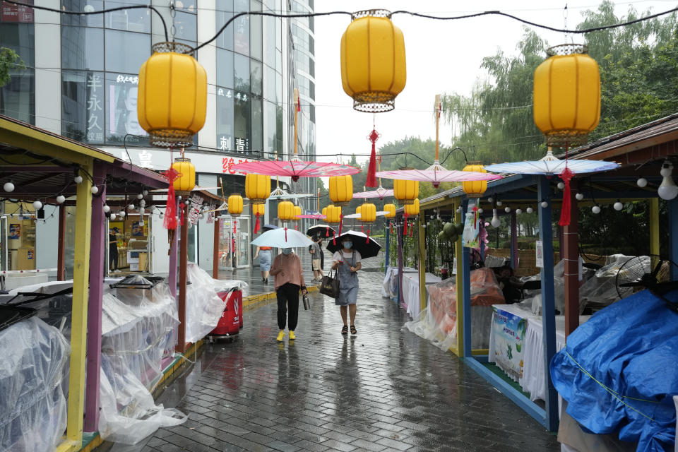 Residents walk near a bazaar closed due to the rain in Beijing, Sunday, Aug. 14, 2022. China’s central bank trimmed a key interest rate Monday to shore up sagging economic growth at a politically sensitive time when President Xi Jinping is believed to be trying to extend his hold on power. (AP Photo/Ng Han Guan)