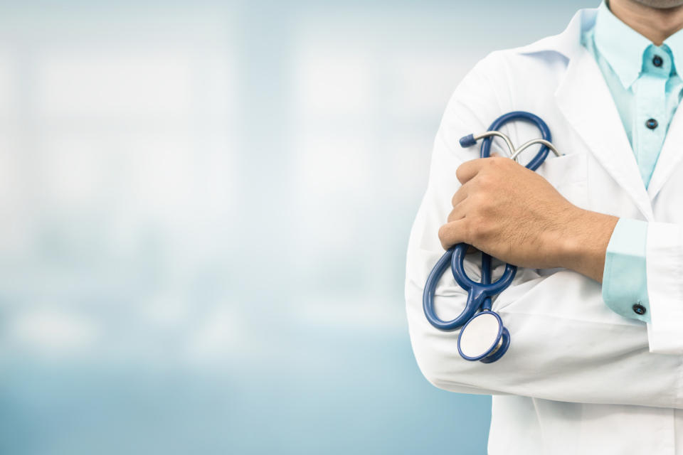 Person in white lab coat holding a stethoscope.