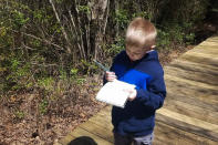 In this April 16, 2020, photo, provided by Dan Cappilla, his son Gavin takes notes for a school project while walking on a nature trail in Tuckerton, N.J. The coronavirus pandemic has created a staggering child care crisis that threatens to undermine the reopening of the U.S. economy. Dan Cappilla saw other no choice but to take unpaid leave from his job as an overnight baker at a ShopRite in Manahawkin, N.J. (Dan Cappilla via AP)