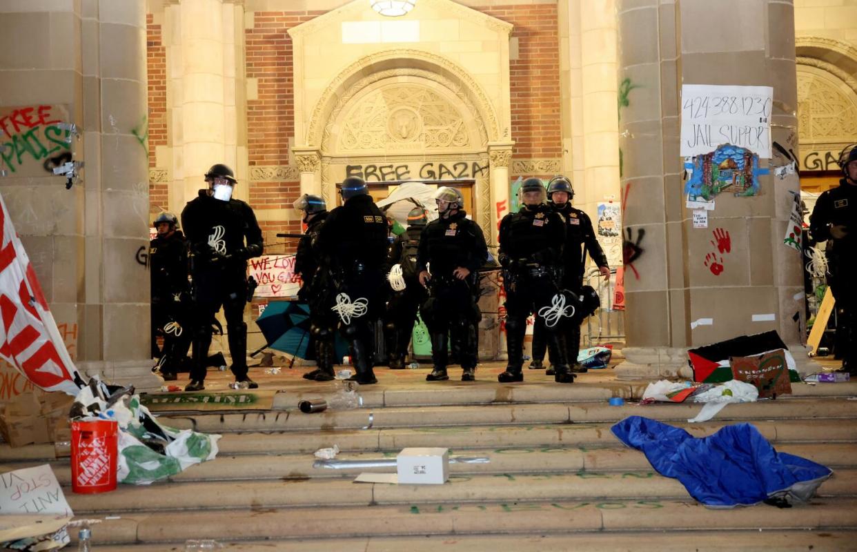 Police at a building on the UCLA campus where debris is scattered on steps and Free Gaza is spray painted on a doorway.